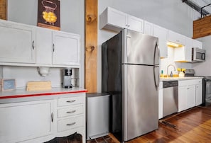 A modern kitchen with stainless steel appliances, white cabinetry, and a wooden accent wall.