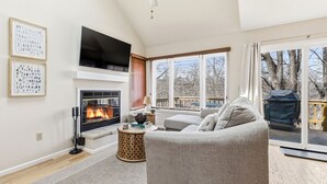 A living room with a fireplace, a sofa, a television, and a view of the outdoors. - King Bed w Pull Out Sofa + Murphy Bed (Galena)