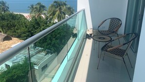 Un balcon doté d’une balustrade en verre, offrant une vue sur une plage et des palmiers.