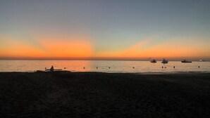 Une plage au coucher du soleil, avec des bateaux et une personne assise sur le sable.