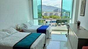 Une chambre d’hôtel avec deux lits, un bureau et une grande fenêtre donnant sur des immeubles et des montagnes.