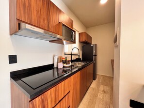 A modern kitchen with wooden cabinets, a black countertop, stainless steel appliances, and a built-in microwave. - Tulum & comfort Travel Apartment 2DB 1BR + Jacuzzi, gym, cinema, swimming pools and more (Tulum)