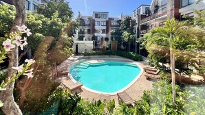 A swimming pool surrounded by lounge chairs and greenery, with modern buildings in the background. - Tulum & comfort Travel Apartment 2DB 1BR + Jacuzzi, gym, cinema, swimming pools and more (Tulum)