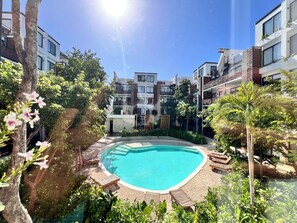 Ein Swimmingpool, umgeben von Liegestühlen und Grünflächen, mit modernen Gebäuden im Hintergrund.