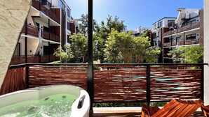 A modern outdoor area with a hot tub, wooden lounge chairs, and a view of multi-story buildings. - Tulum & comfort Travel Apartment 2DB 1BR + Jacuzzi, gym, cinema, swimming pools and more (Tulum)