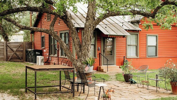 Una casa in legno rossa con patio, posti a sedere all'aperto e un albero.