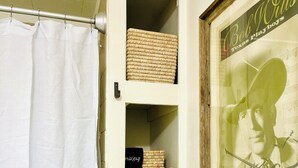 Un bagno con una tenda da doccia bianca, un quadro con l'immagine di una figura storica, e mensole con asciugamani e cesti.