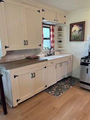 A kitchen with light-colored cabinets, a stainless steel stove, and a floral-patterned rug.