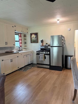 Une cuisine avec des meubles de rangement en bois, une cuisinière, un réfrigérateur et une poubelle.
