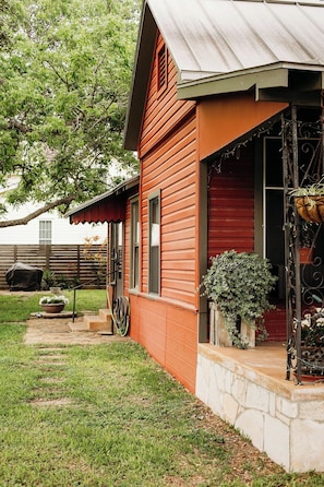 Une maison en bois rouge, dotée d’un porche, d’un jardin et d’un toit en métal.