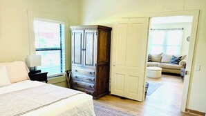 Una camera da letto con un letto, un armadio, un comodino, una finestra e una porta che dà su un soggiorno.