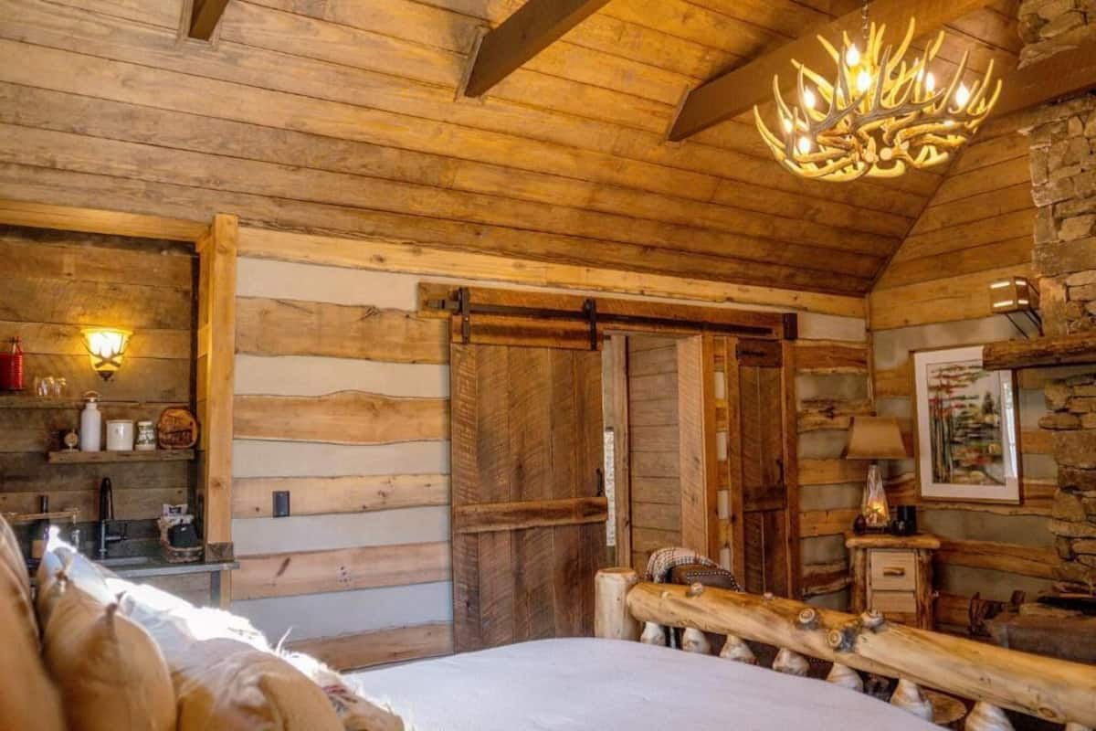 L’intérieur d’une cabane en rondins, avec un lit, des murs en bois, un lustre et une cheminée.