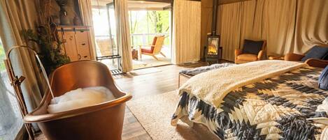 Un dormitorio con una cama grande, una bañera de madera, una silla y una chimenea.