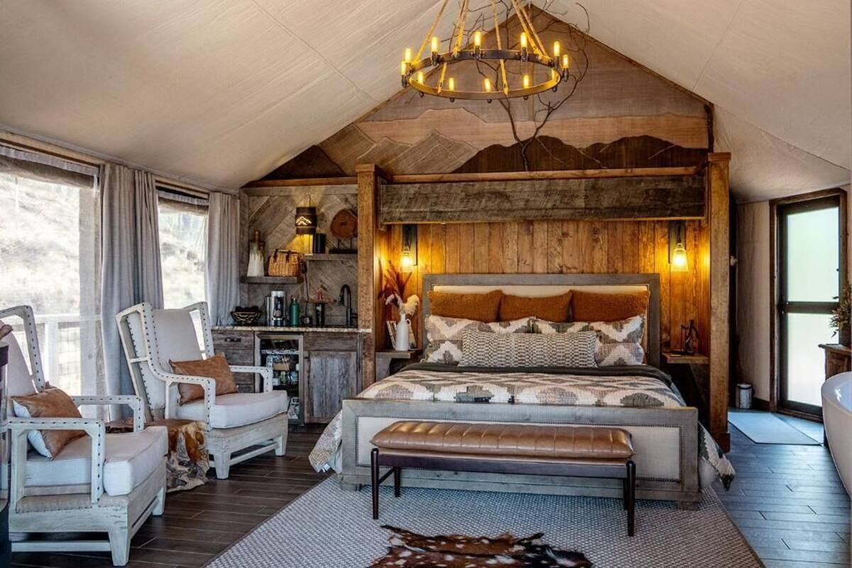 Une chambre à coucher avec un grand lit, deux fauteuils, un banc, un lustre et un plafond en bois rustique.