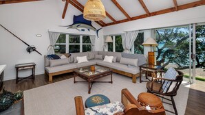 A spacious living area with a large sofa, a coffee table, and a view of the outdoors. - Te Uenga - Parekura Bay Holiday Home (Parekura Bay)