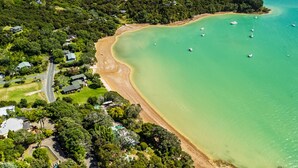 An aerial view of a coastal area with a beach, boats, and scattered houses. - Te Uenga - Parekura Bay Holiday Home (Parekura Bay)