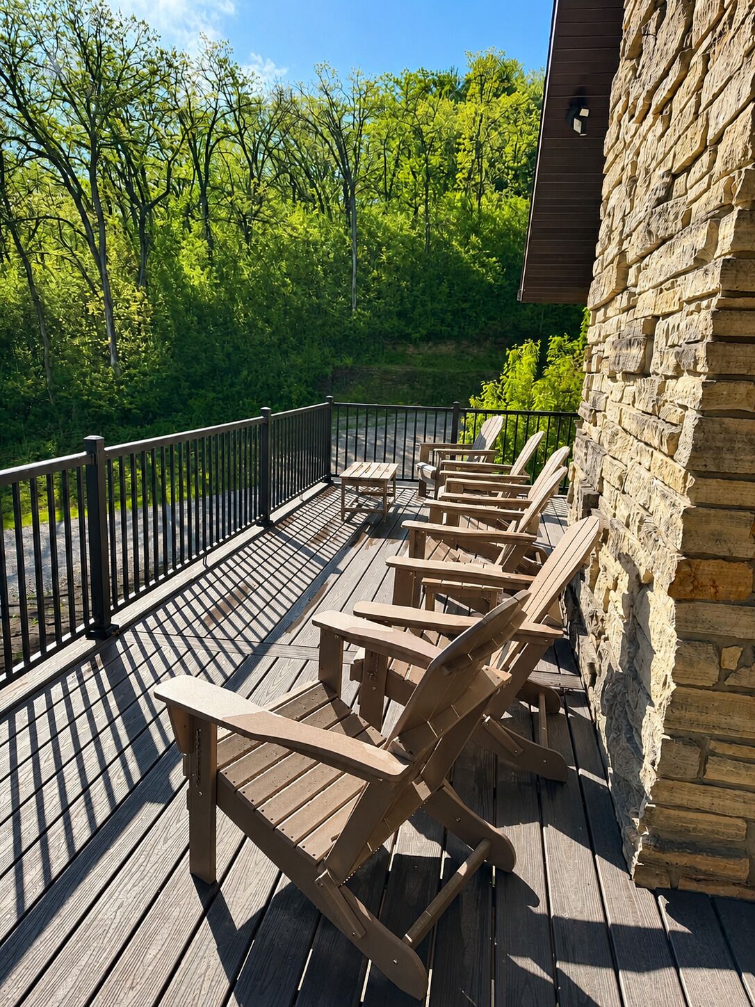 Una terraza de madera con sillas Adirondack, un muro de piedra y vistas a un bosque.