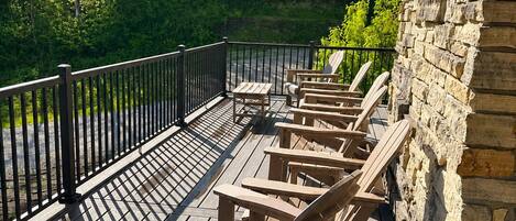 Una terraza de madera con sillas Adirondack, un muro de piedra y vistas a un bosque.