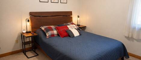 A bedroom with a bed, bedside tables, a headboard, and wall-mounted artwork.