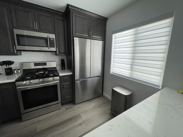 A modern kitchen with stainless steel appliances, dark cabinetry, and a window with blinds.