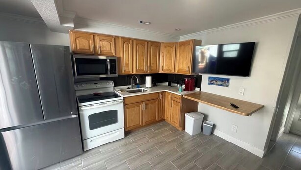 Een moderne keuken met roestvrijstalen apparatuur, houten keukenkastjes en een flatscreen televisie boven de aanrecht.