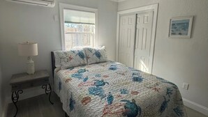 Een slaapkamer met een bed, een plafondventilator, een raam, een deur en een nachtkastje.
