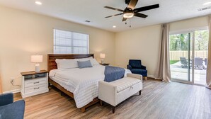A bedroom with a bed, bedside tables, a chair, a ceiling fan, and a view of the outdoors.