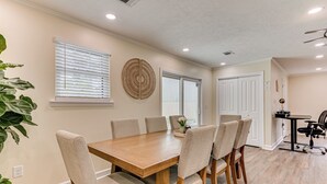 A dining area with a wooden table and six chairs, a potted plant, and a window with blinds.