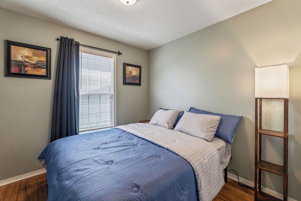 A bedroom with a bed, a nightstand, a lamp, and two framed pictures on the wall.