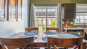 A dining area with a table set for four, wooden chairs, a kitchen with a dishwasher, and a view through a glass door to the outside. - Blue Moon Ranch in Bloomington (Bloomington)