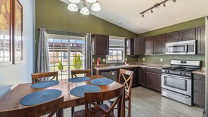 A kitchen with dark cabinets, a stainless steel stove, and a dining area with wooden chairs and placemats. - Blue Moon Ranch in Bloomington (Bloomington)