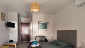 A hotel room with a bed, a desk, a chair, a television, and a painting on the wall. - Seaside studio in Moriani (San-Nicolao)