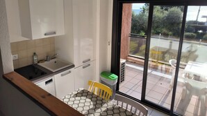 A modern kitchen with white cabinets, a built-in sink, and a dining area with a patterned table and chairs. - Seaside studio in Moriani (San-Nicolao)