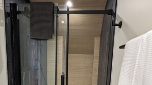 Ein modernes Badezimmer mit einer Duschkabine aus Glas, einem Holzausleger und einem weißen Handtuch.