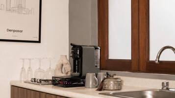 Cozinha com cafeteira, copos de vinho e uma pintura de paisagem urbana emoldurada.