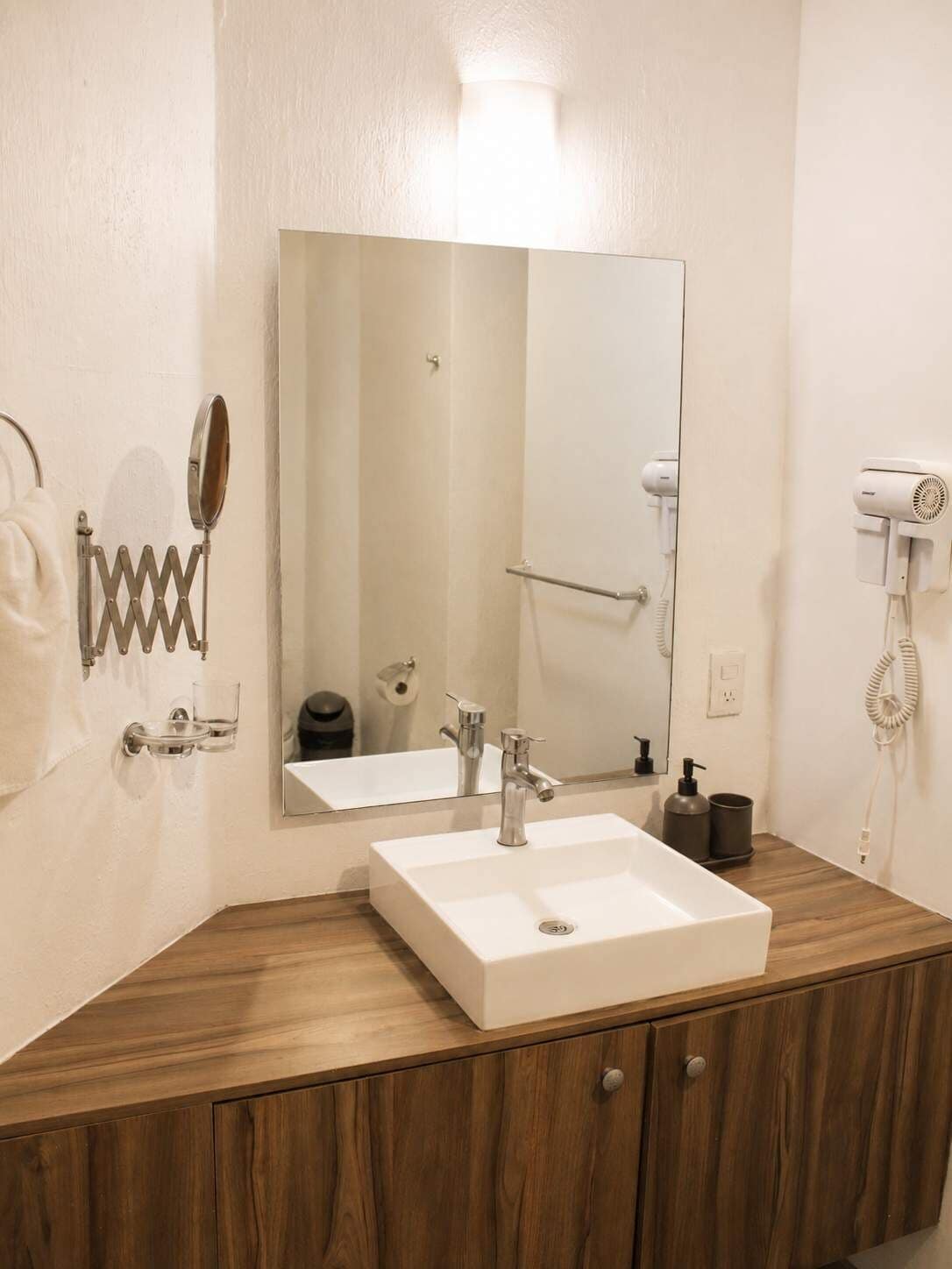 Un baño con lavamanos blanco, un espejo, toallero, secador de pelo y dispensador de papel higiénico.