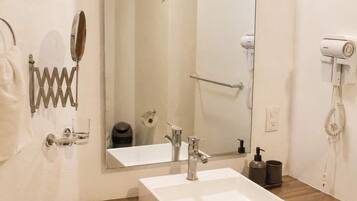 Un baño con lavamanos blanco, un espejo, toallero, secador de pelo y dispensador de papel higiénico.