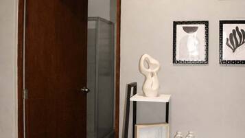 Um quarto com porta de madeira, uma mesa branca com um vaso, obras de arte emolduradas e uma cadeira.