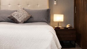 A bedroom with a tufted headboard, a bedside lamp, and a wooden wardrobe. - Suite Privada Totalmente Equipada (Zapopan)