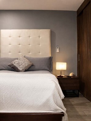 Ein Schlafzimmer mit einer gepolsterten Kopfstütze, einer Nachttischlampe und einem Holzschrank.