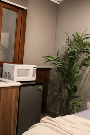 Eine kleine Küchenzeile mit einer Mikrowelle, einem Kühlschrank und einem Blumentopf.