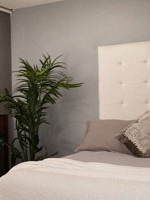 Ein Schlafzimmer mit einer gesteppten Kopfteile, einer großen Kübelpflanze und einem Bett mit einer strukturierten weißen Bettdecke.