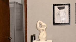 A room with a white table, a framed picture, a white vase, and two water bottles. - Suite Privada Totalmente Equipada (Zapopan)