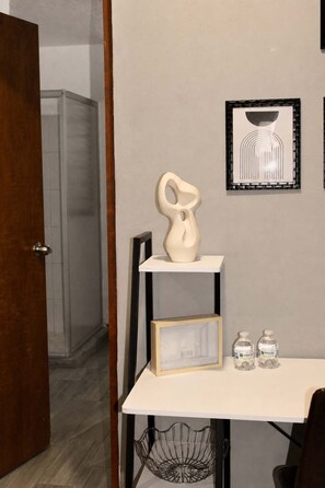 Ein Zimmer mit einem weißen Tisch, einem gerahmten Bild, einer weißen Vase und zwei Wasserflaschen.