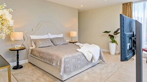 Un dormitorio moderno con una cama grande, dos mesitas de noche, un televisor de pantalla plana y una planta en maceta.