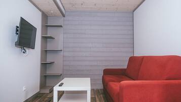A room with a white sofa, a small white table, a mounted TV, and a grey wall with wooden paneling.