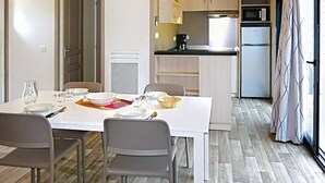 Een compacte keuken met moderne apparaten, een eethoek met een tafel voor vier personen, en uitzicht door een raam.