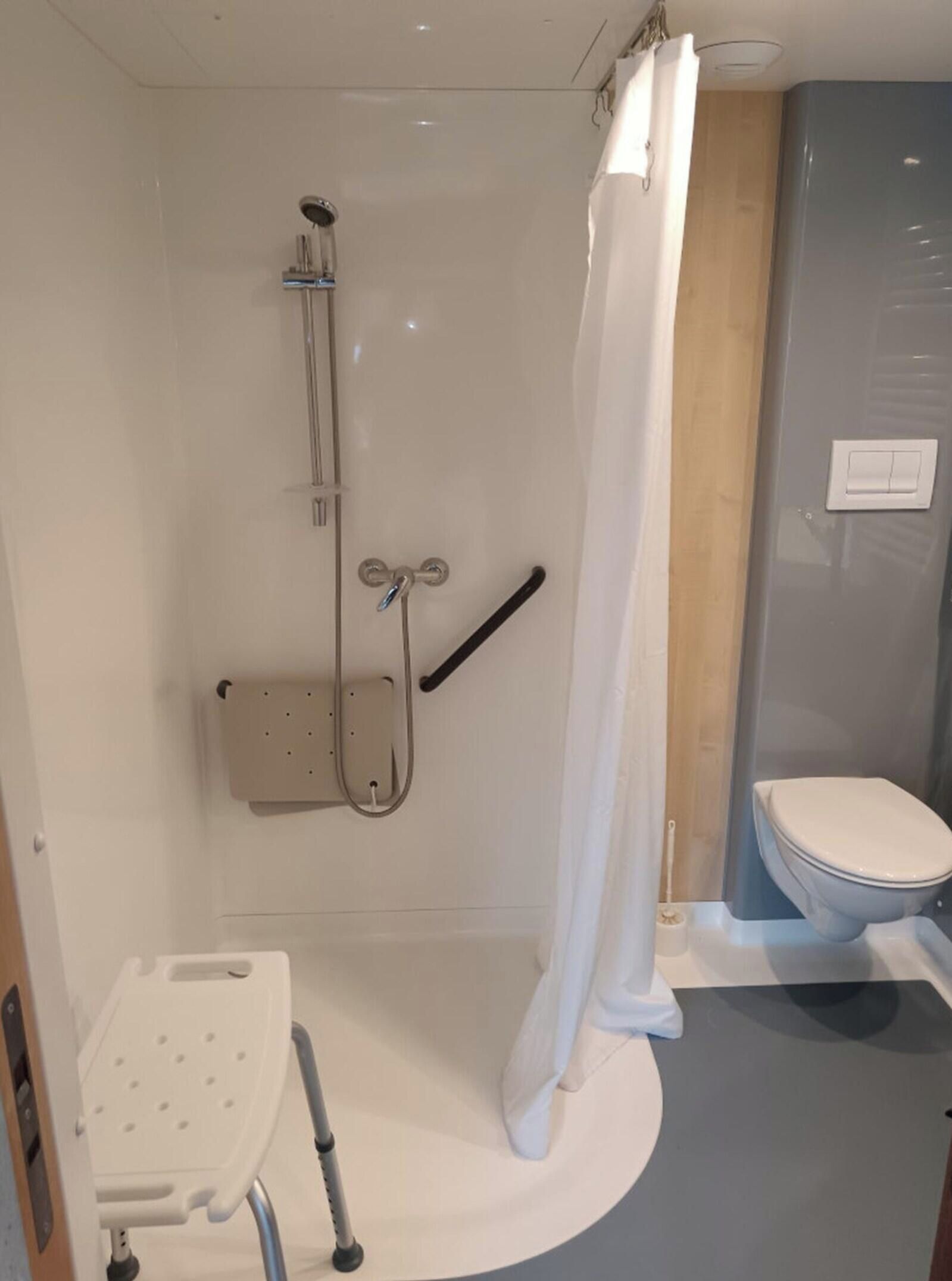 Een badkamer met douche, toilet en een bankje voor rolstoelgebruikers.