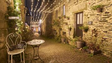 A stone building with a cobblestone courtyard, a white metal chair, a round table, and string lights.