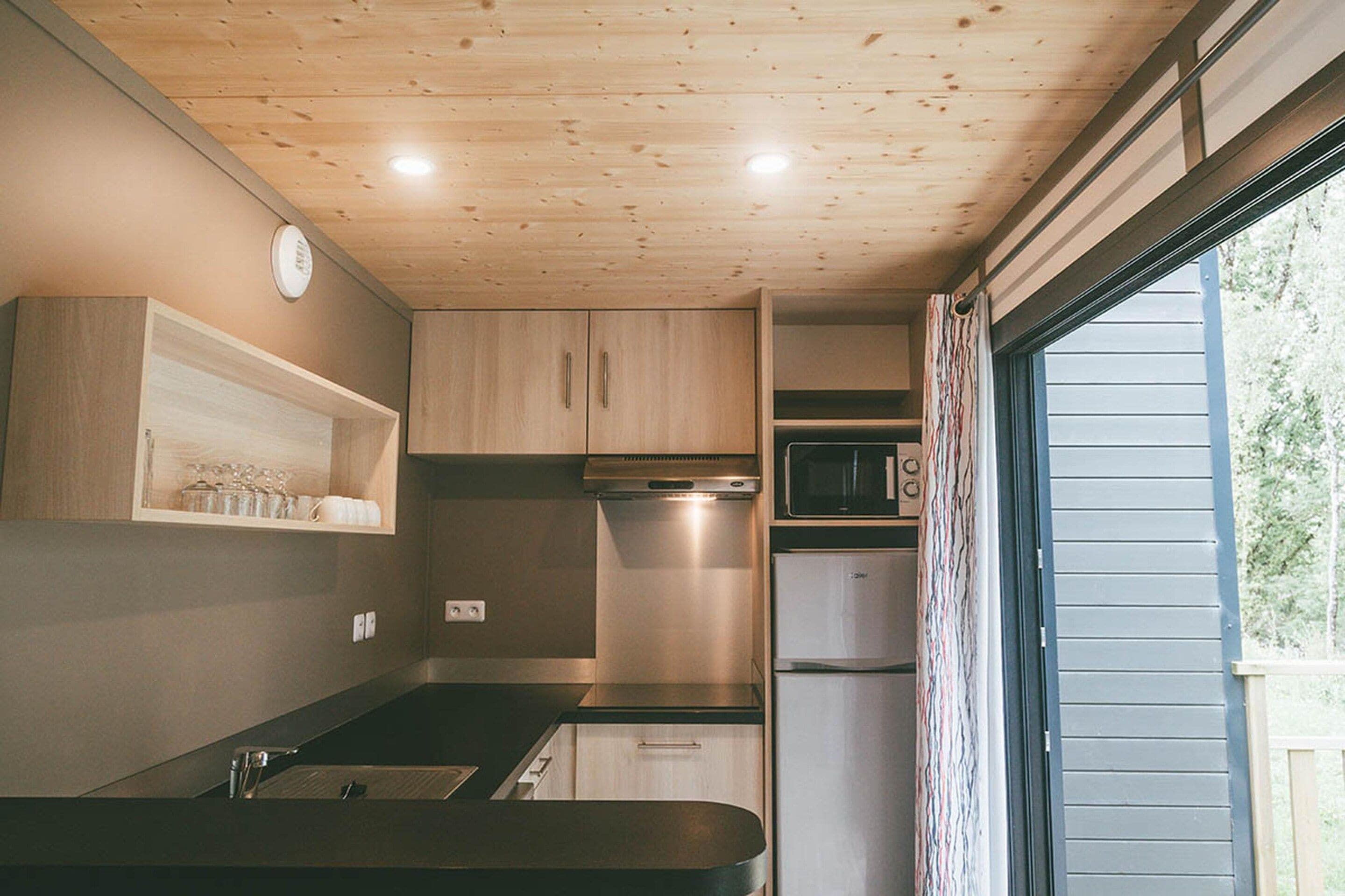 A compact kitchen with wooden cabinets, a microwave, and a small refrigerator.